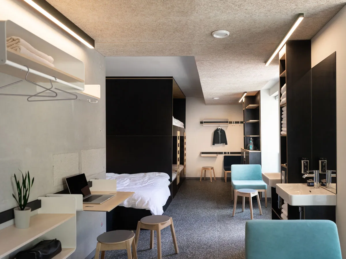 Hostelzimmer mit Etagenbett, Klapptisch und Ablagen an der Wandleiste