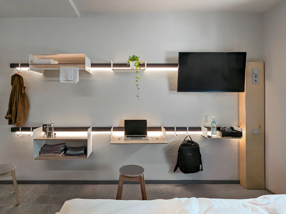 Zwei Wandleisten tragen Ablagen, Haken, Klapptisch und Fernseher