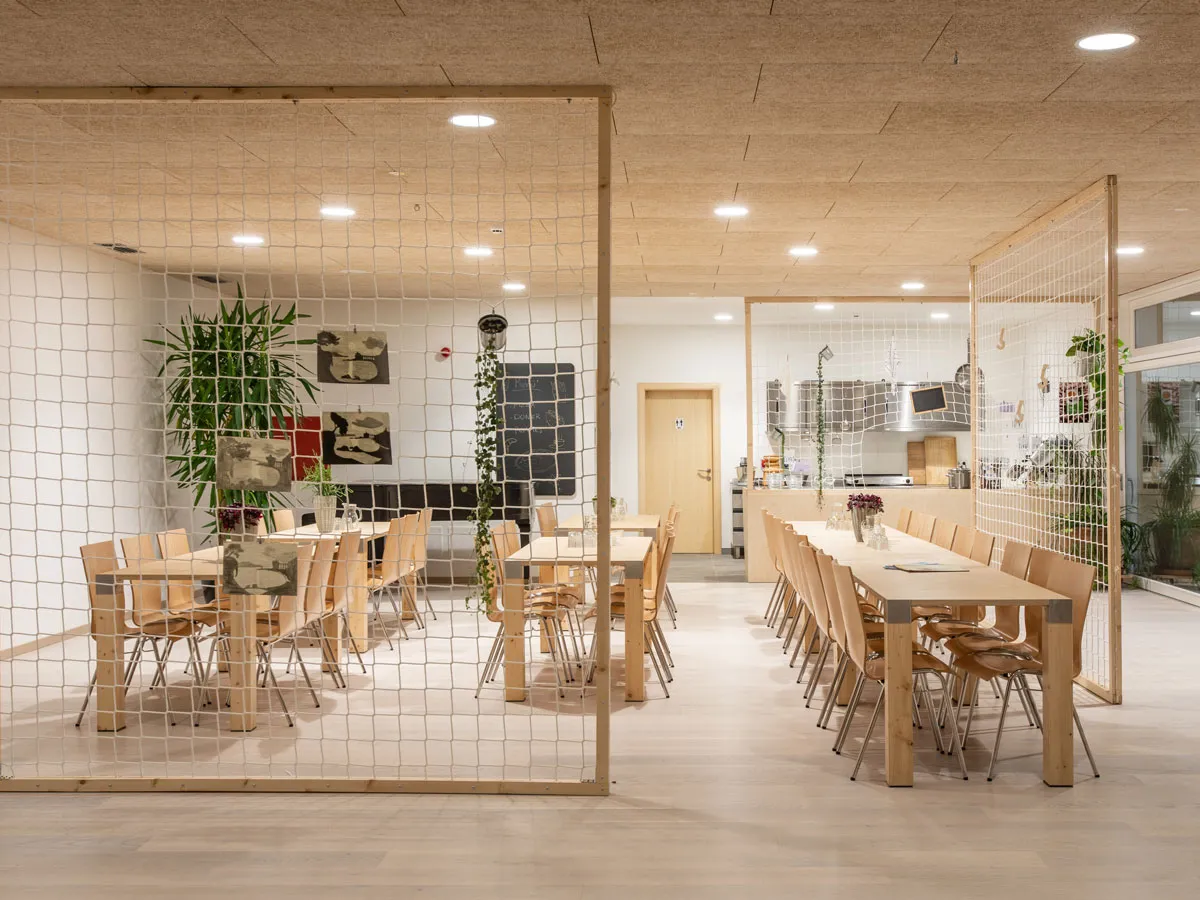 Speisesaal mit langen Holztischen und Netz-Raumteilern