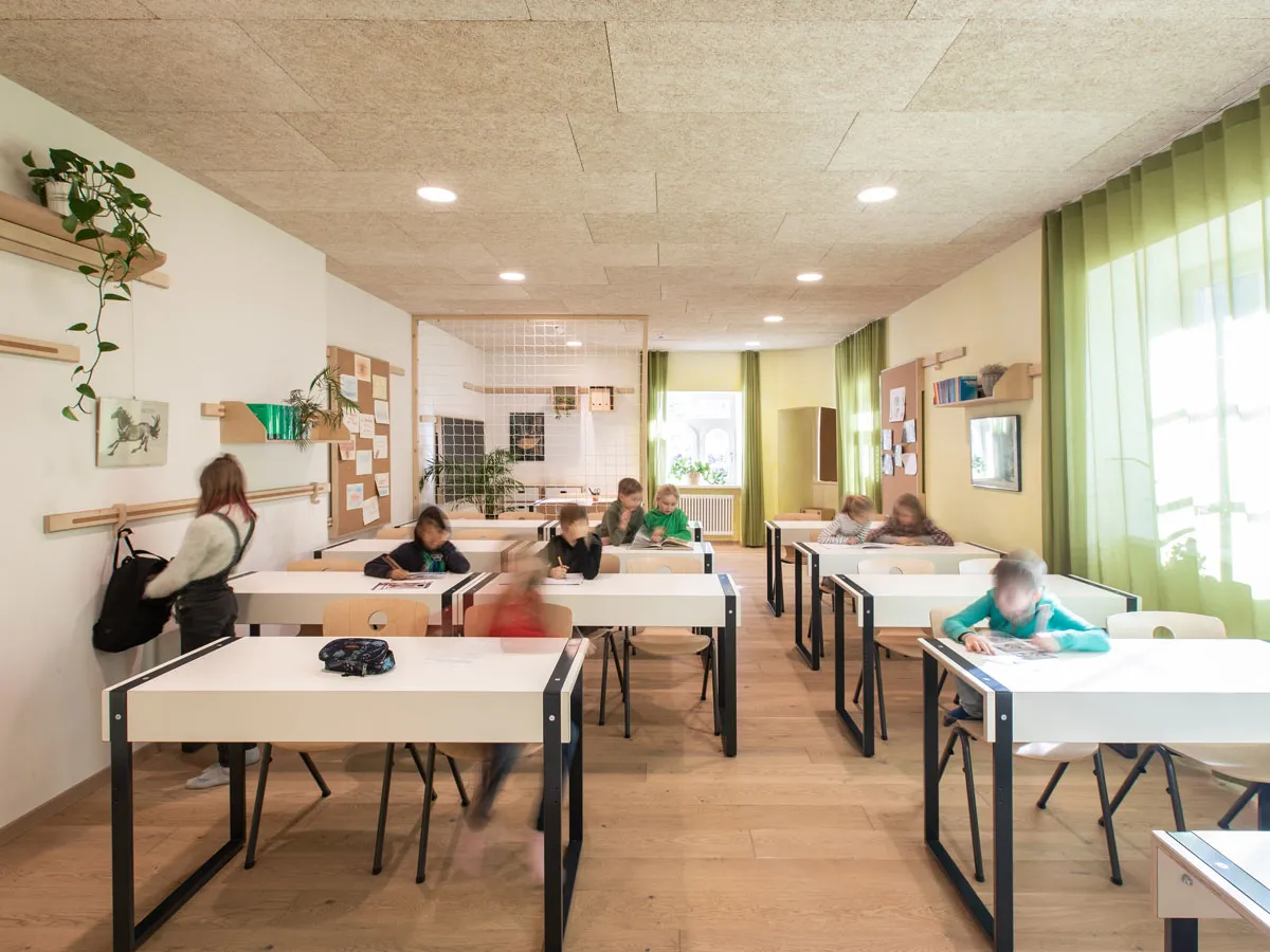 Klassenzimmer mit Schülertischen, Pinnwand und Haken an der Wandleiste